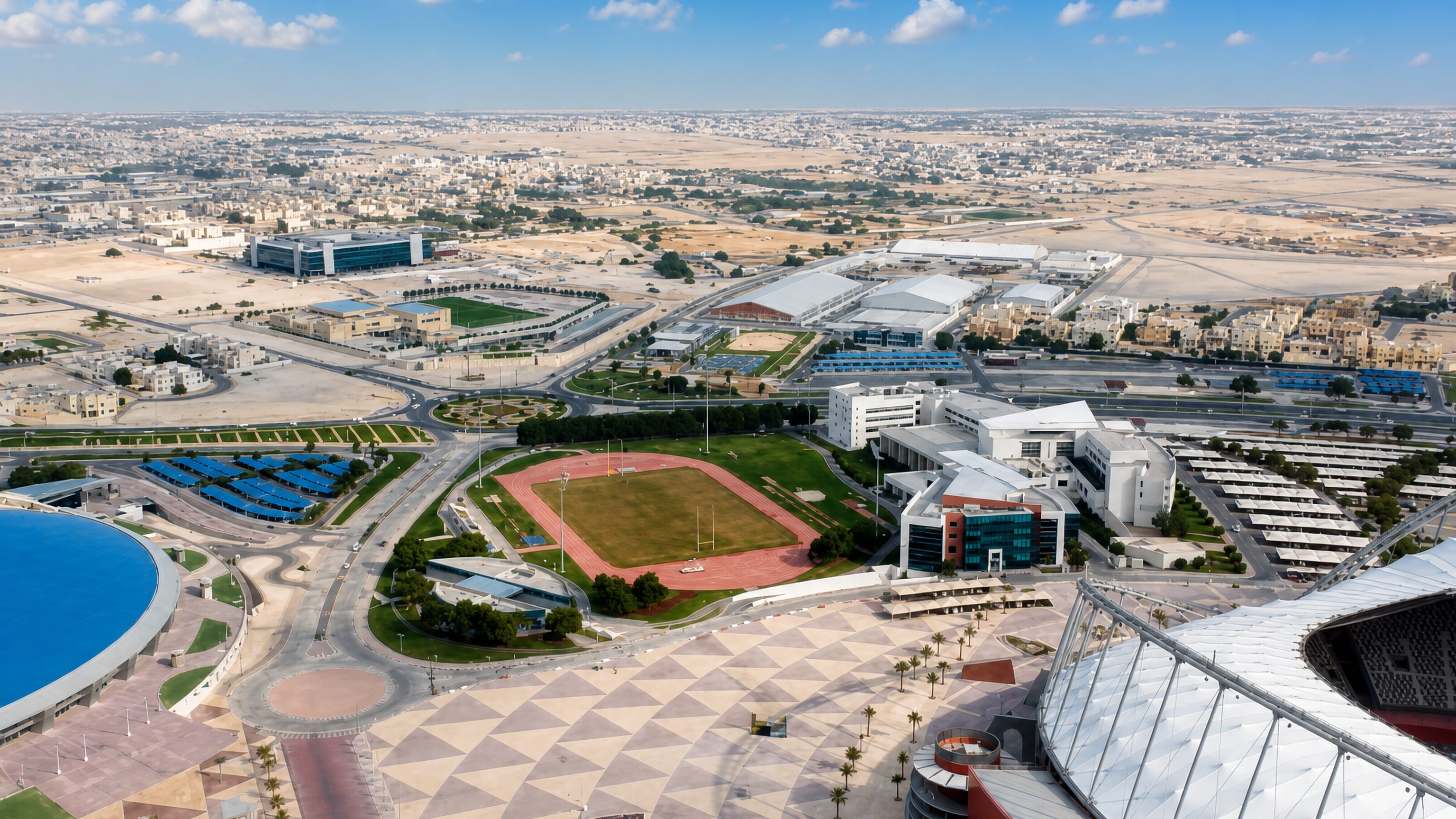 Aerial view over Al Rayyan, Qatar, with the Aspire Zone dome, stadium roof and desert suburbs beyond