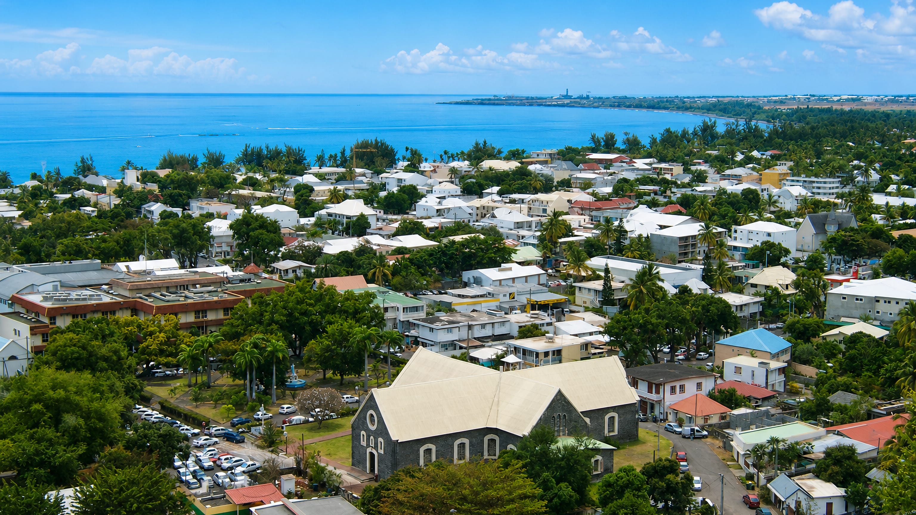 Aerial view of Saint-Paul, Réunion, its stone church and rooftops set along the curving Indian Ocean shore.