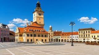 Braşov's Council Square with the Casa Sfatului clock tower, pastel merchant houses and café terraces in sunshine