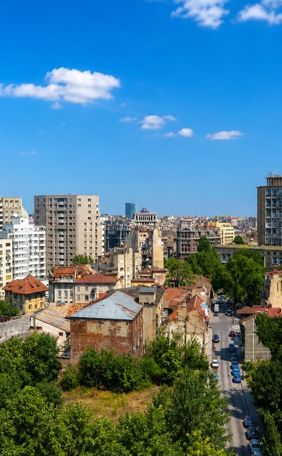 Bucharest cityscape of mixed communist-era apartment blocks and older buildings among trees, Romania.
