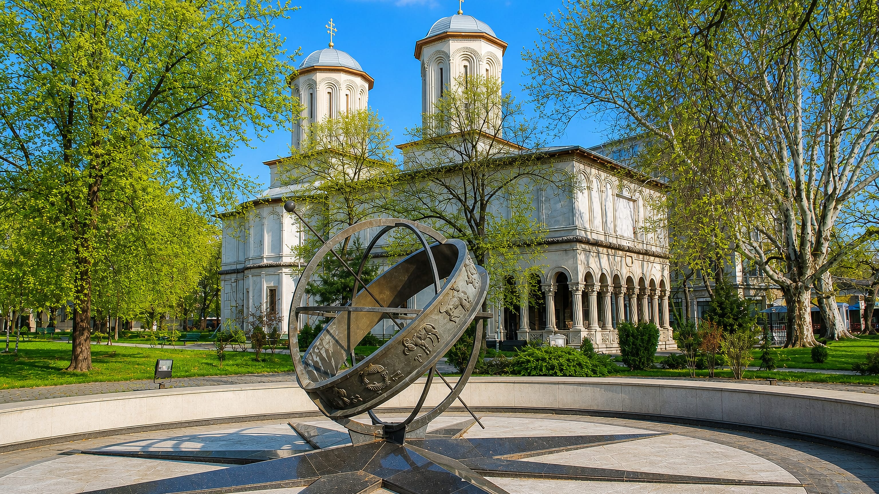 White twin-domed Orthodox church behind an armillary sphere sculpture on a paved plaza in Sector 3, Bucharest.