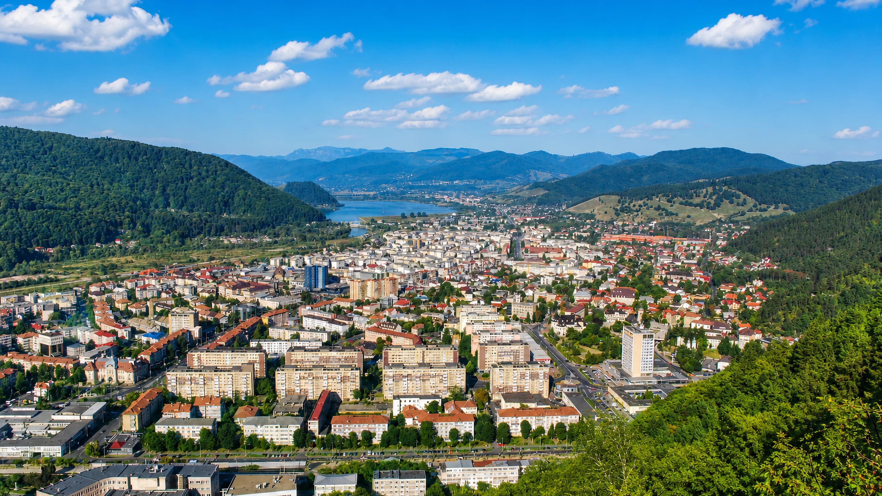 Piatra Neamt filling the Bistrita valley below forested Carpathian hills, with the river lake upstream.