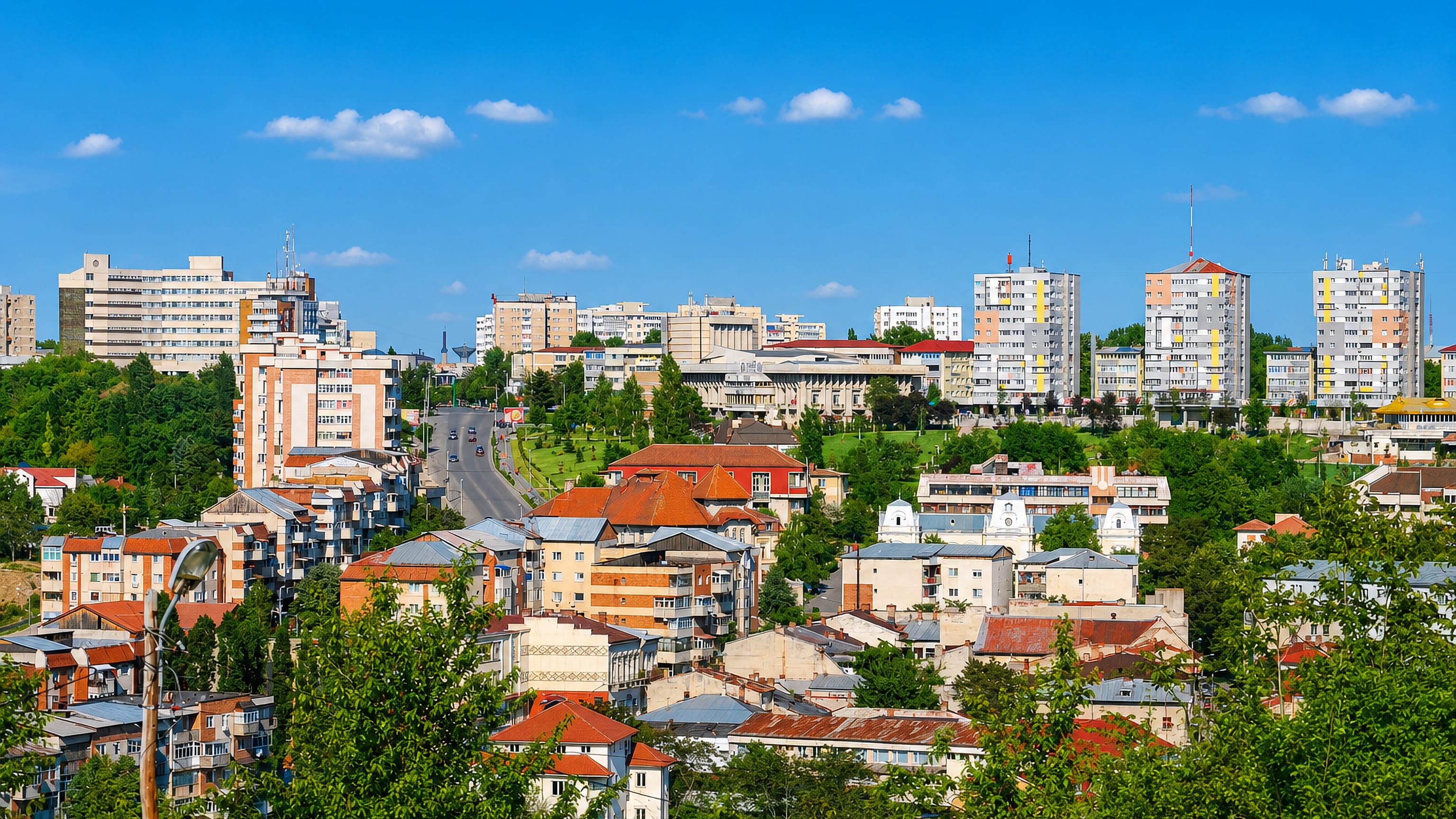 Hillside view over Slatina, Romania, with red-tiled houses below socialist-era apartment blocks.