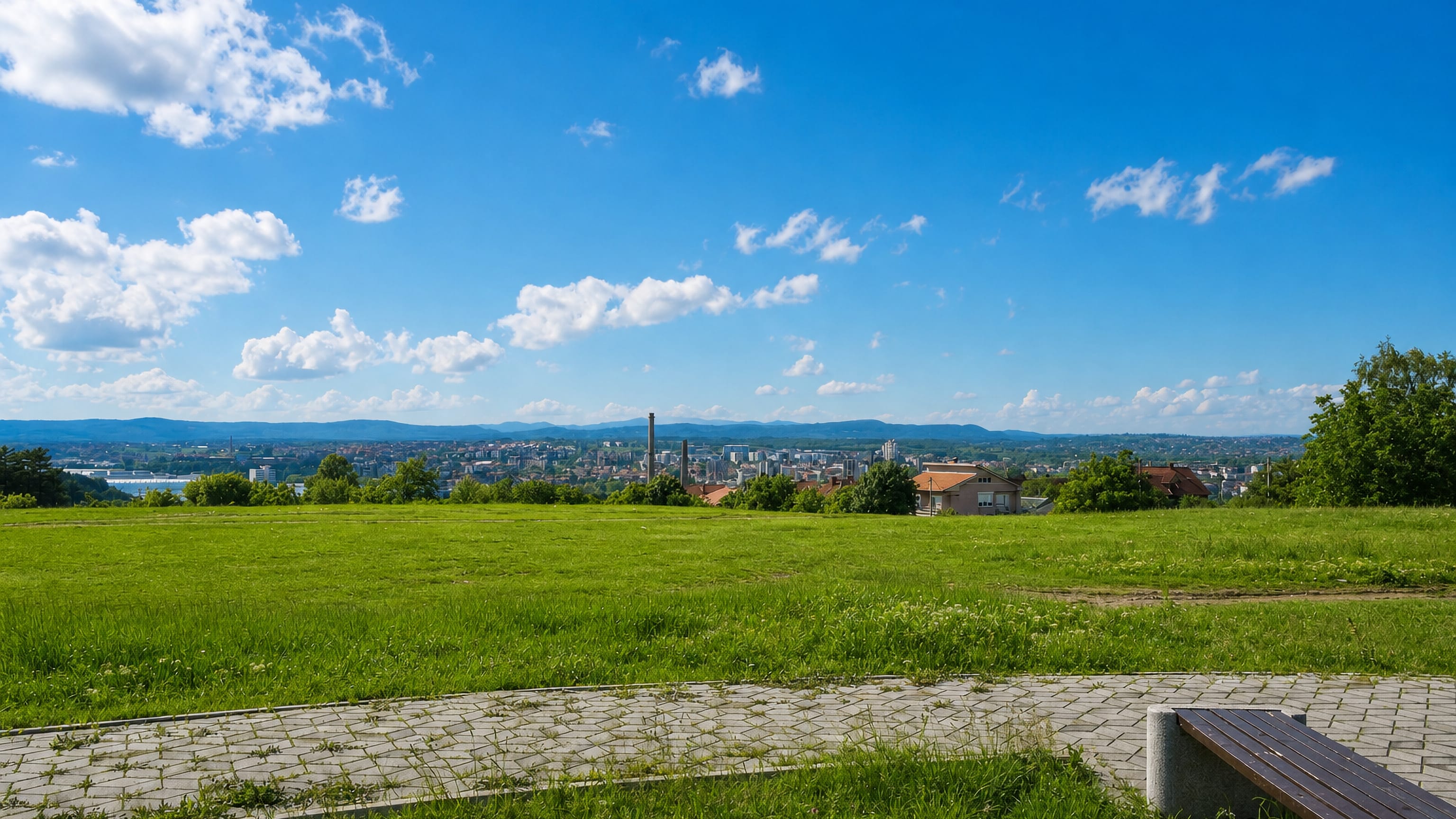 Kragujevac's rooftops and factory chimneys seen across a grassy hilltop park in central Serbia.