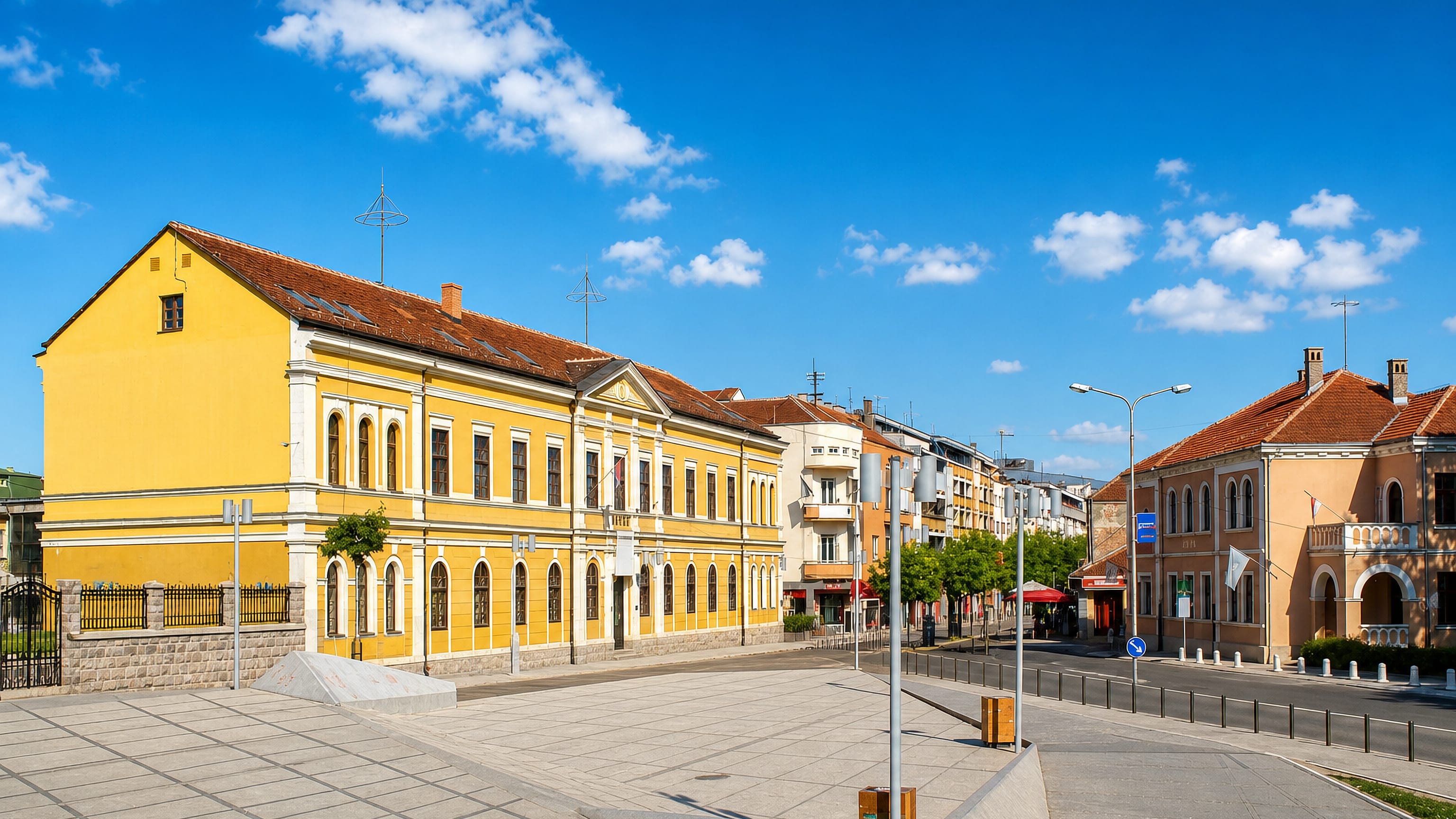 A yellow neoclassical civic building beside the paved central square of Kraljevo, Serbia.