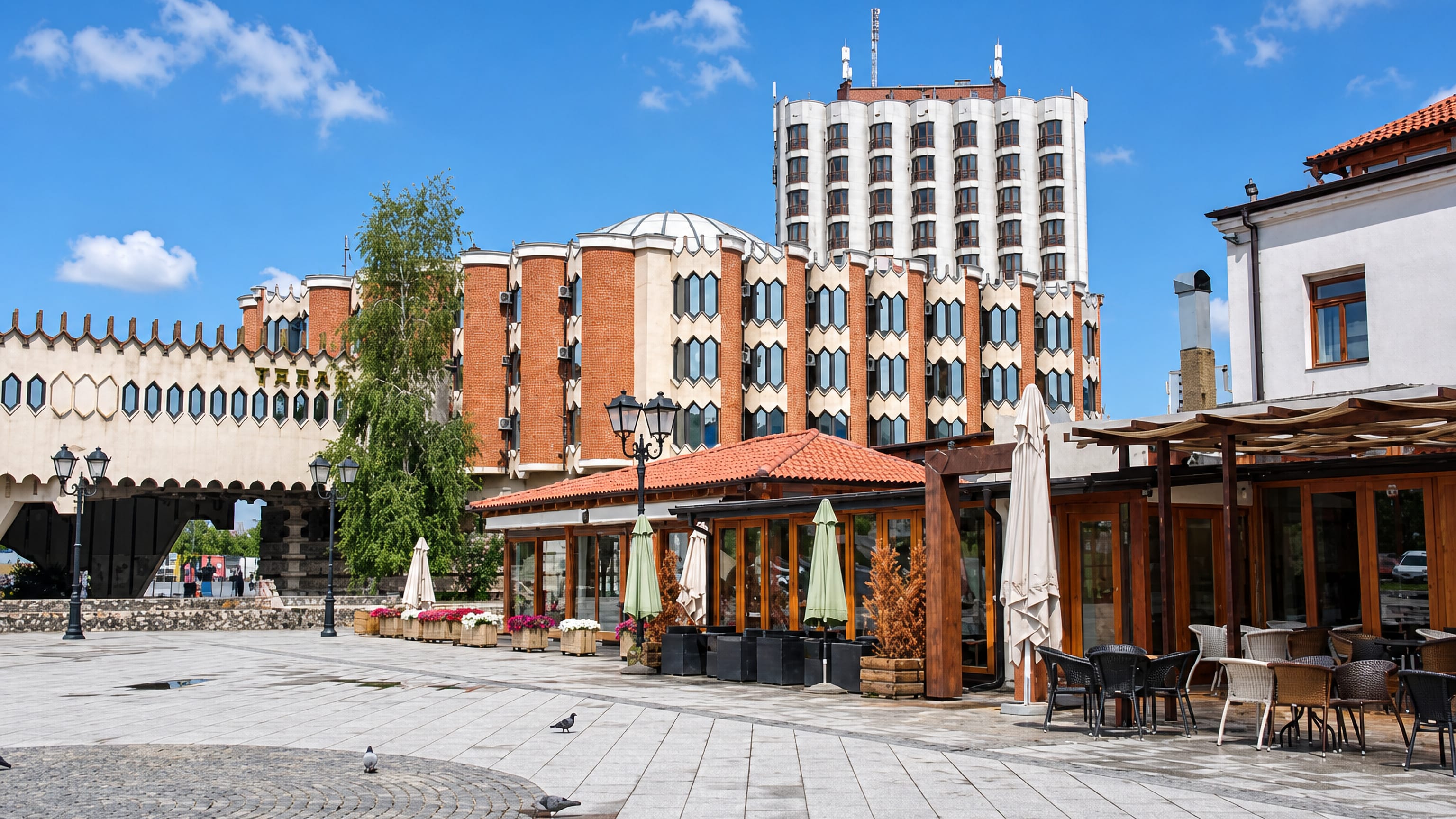 Novi Pazar's Hotel Vrbak, with hexagonal windows and its raised walkway, above a paved square and café terraces.