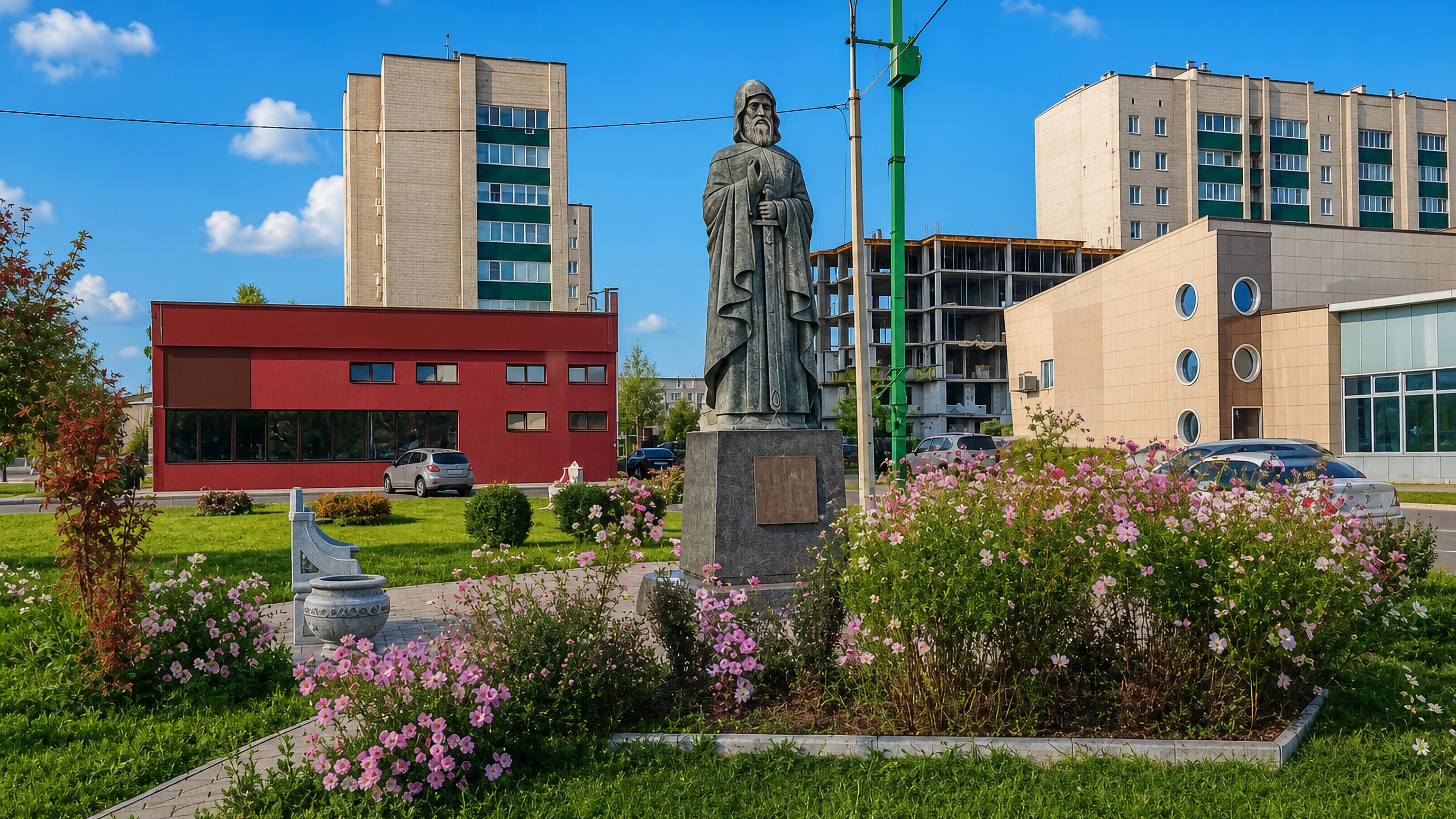 Flowerbeds and a bronze statue on a square in Rubtsovsk, Russia, framed by apartment blocks and a red civic building.