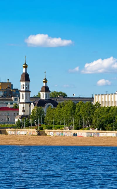 Arkhangelsk waterfront across the Northern Dvina with a white church, embankment and Soviet-era buildings.