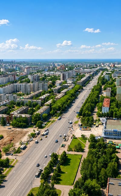 Aerial view of Ufa's wide central avenue lined with apartment blocks and green trees under blue sky.