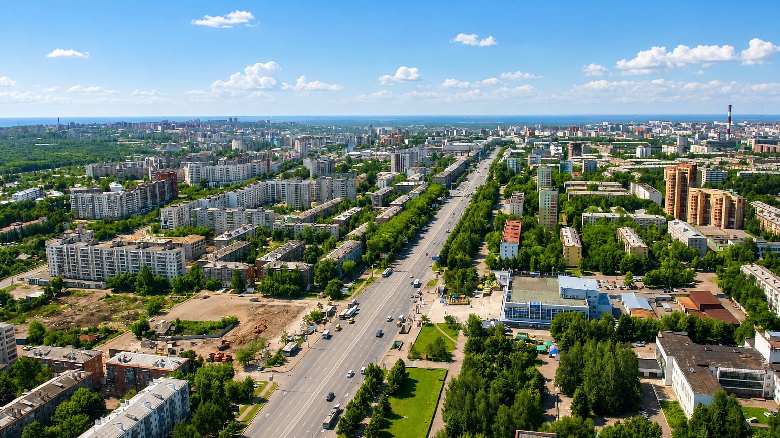 Aerial view of Ufa's wide central avenue lined with apartment blocks and green trees under blue sky.