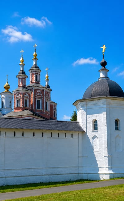 Whitewashed walls and golden-domed churches of Svensky Monastery under a blue summer sky in Bryansk, Russia.