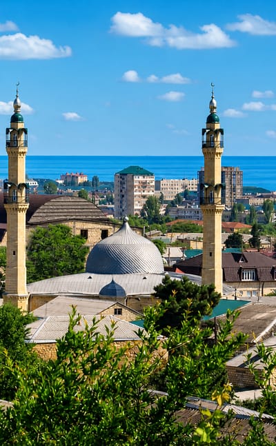 Minarets and dome of the Juma Mosque above Derbent's old-town rooftops with the Caspian Sea beyond, Dagestan.