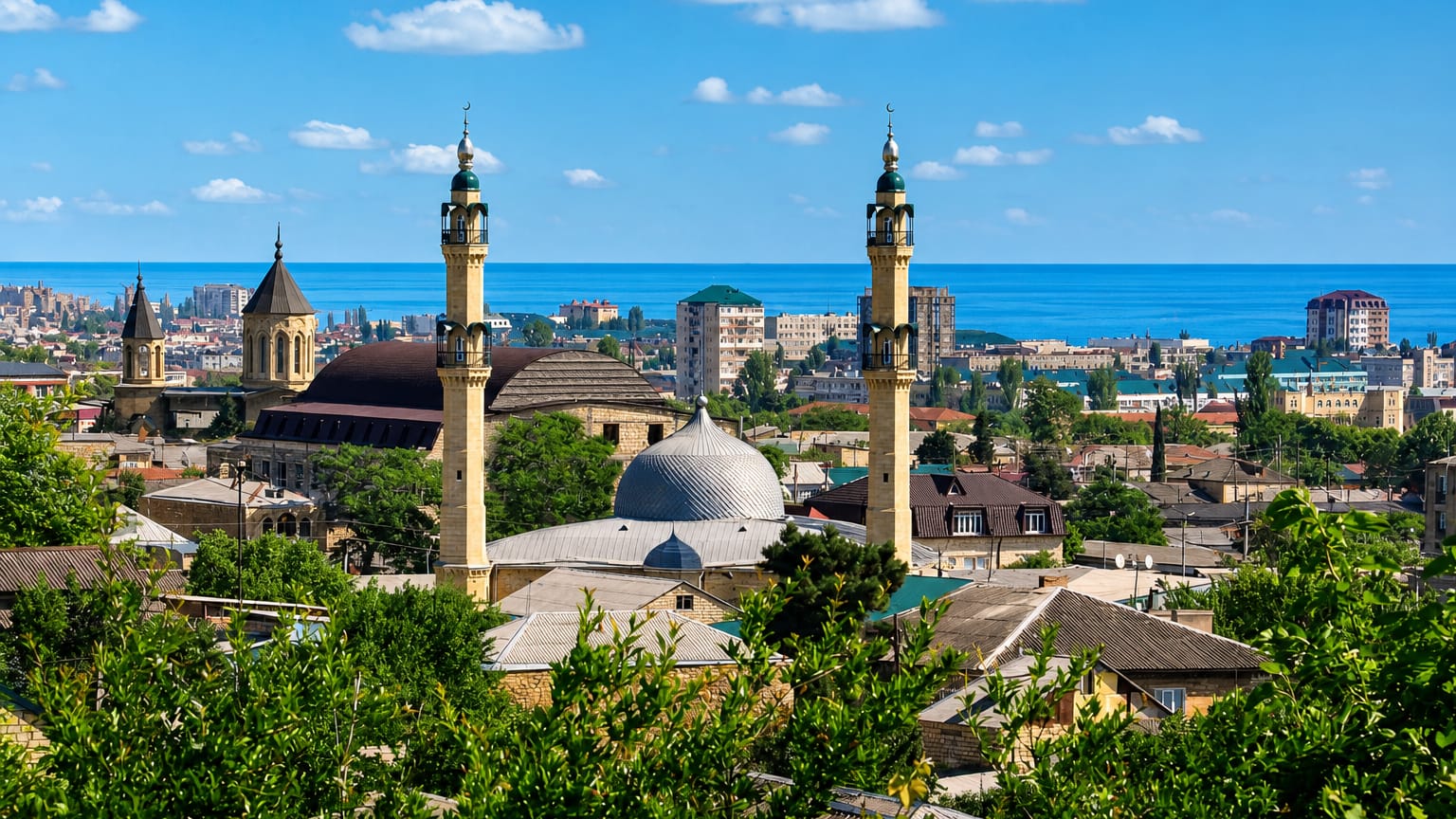 Minarets and dome of the Juma Mosque above Derbent's old-town rooftops with the Caspian Sea beyond, Dagestan.