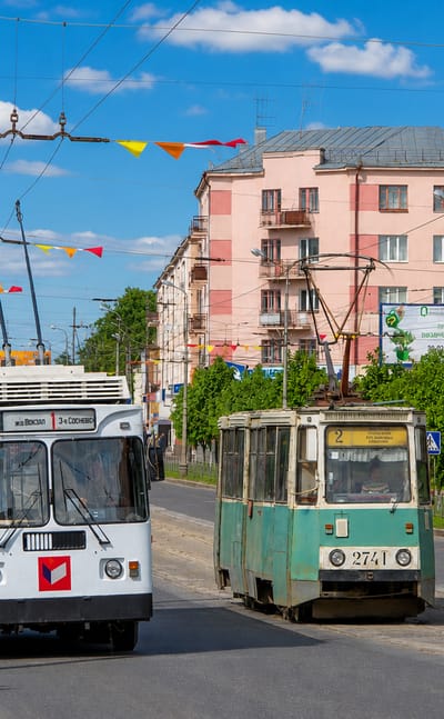 Ivanovo street scene with a white trolleybus and tram passing pastel apartment buildings under festive flags.