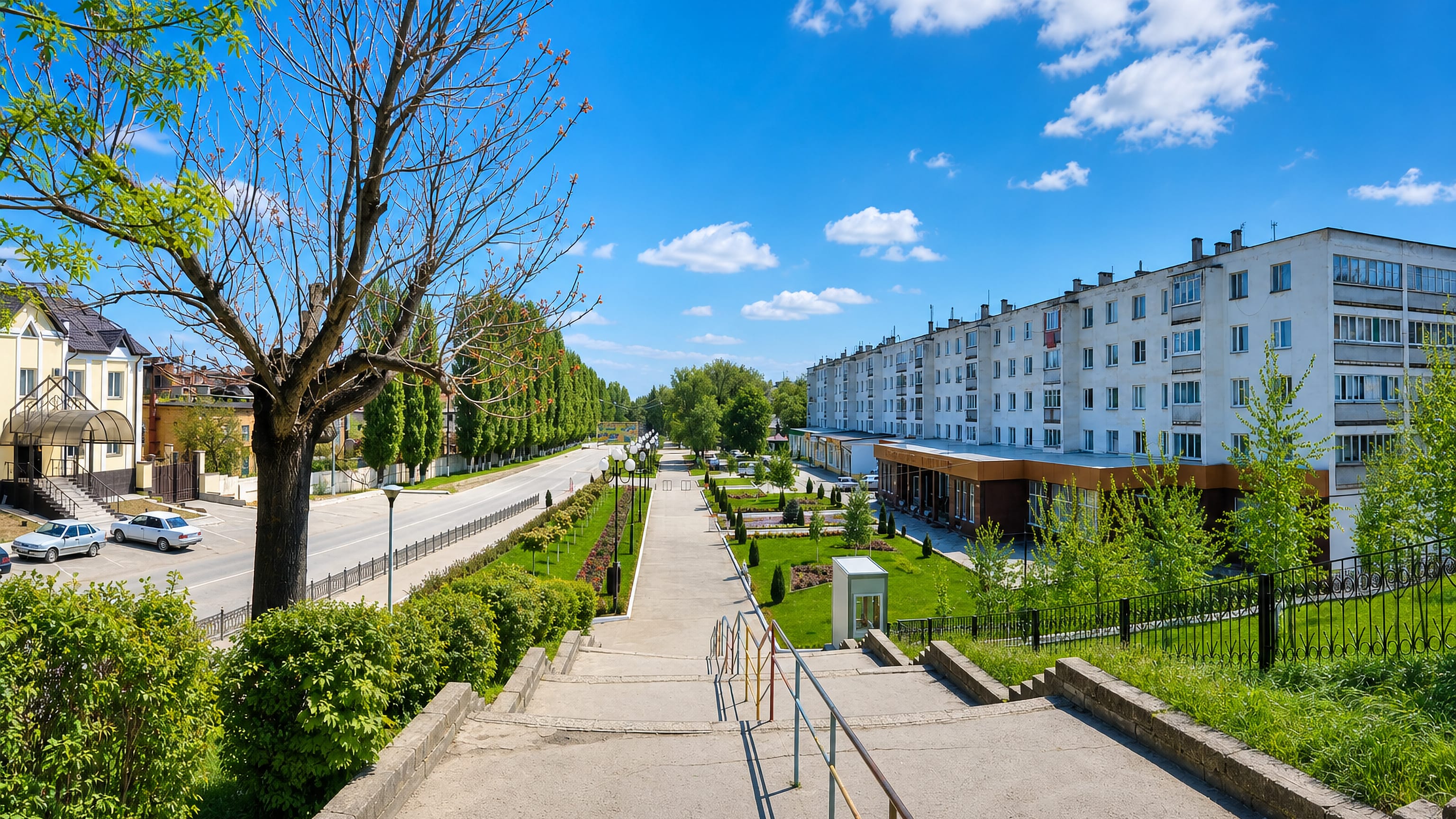 Tree-lined promenade and five-storey apartment blocks along a sunny boulevard in Prokhladnyy, Russia.