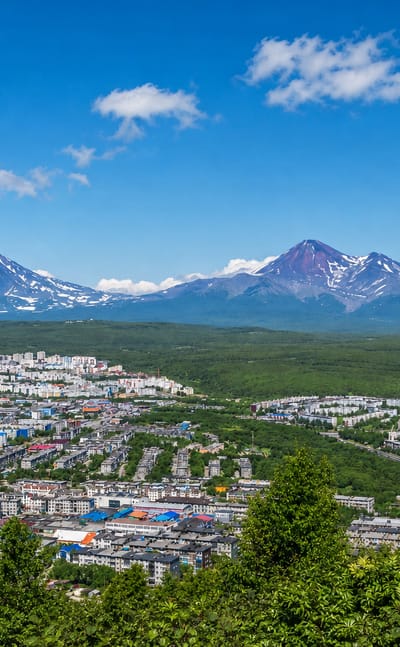 Petropavlovsk-Kamchatsky spread below the snow-streaked Avacha volcanoes under a blue sky
