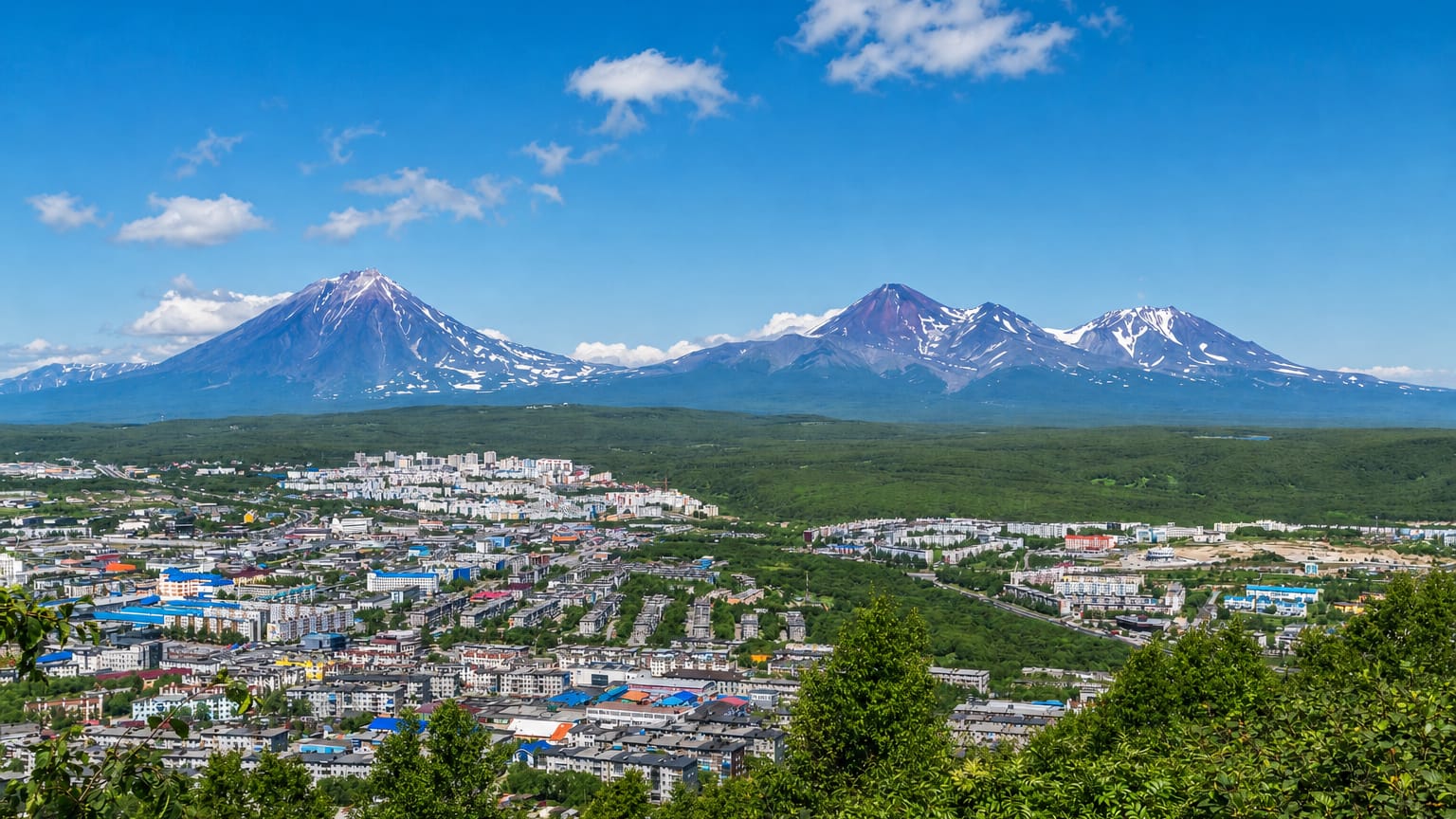 Petropavlovsk-Kamchatsky spread below the snow-streaked Avacha volcanoes under a blue sky
