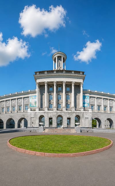 Grand columned Stalinist university building framed by fir trees and a circular lawn in Kemerovo, Russia.