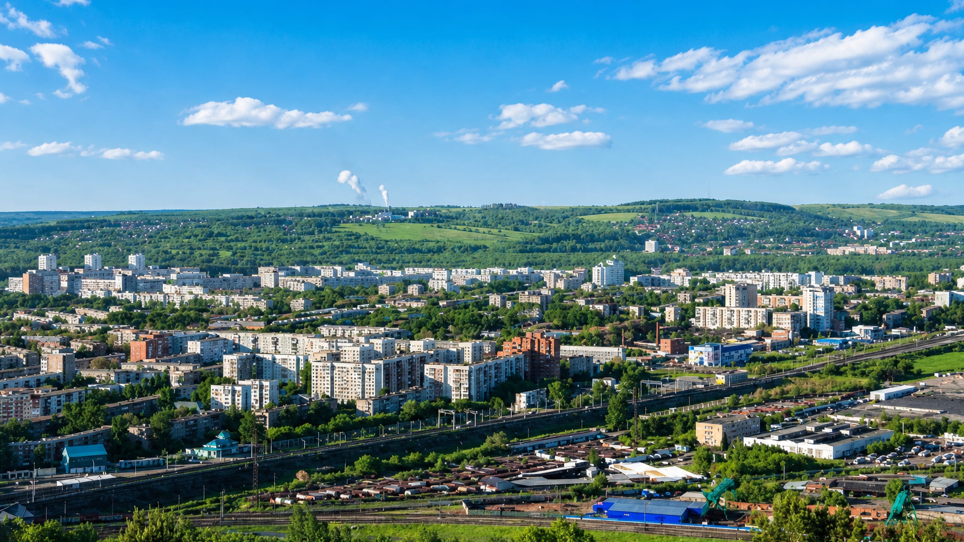 Novokuznetsk from a hillside: Soviet-era apartment blocks, freight rail yards and green Kuznetsk Basin hills.