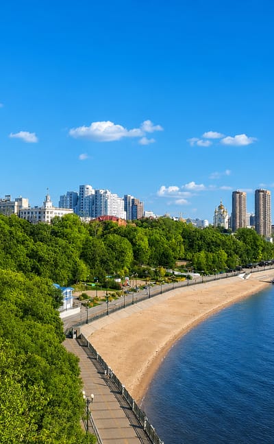 Khabarovsk's Amur River embankment with a sandy city beach, blue-domed cathedral and riverside towers.