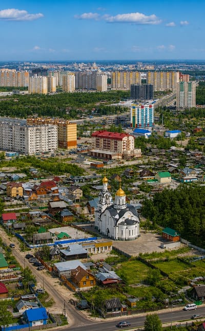 Aerial view of Surgut, Russia, with a white golden-domed church, wooden houses and apartment blocks by forest.