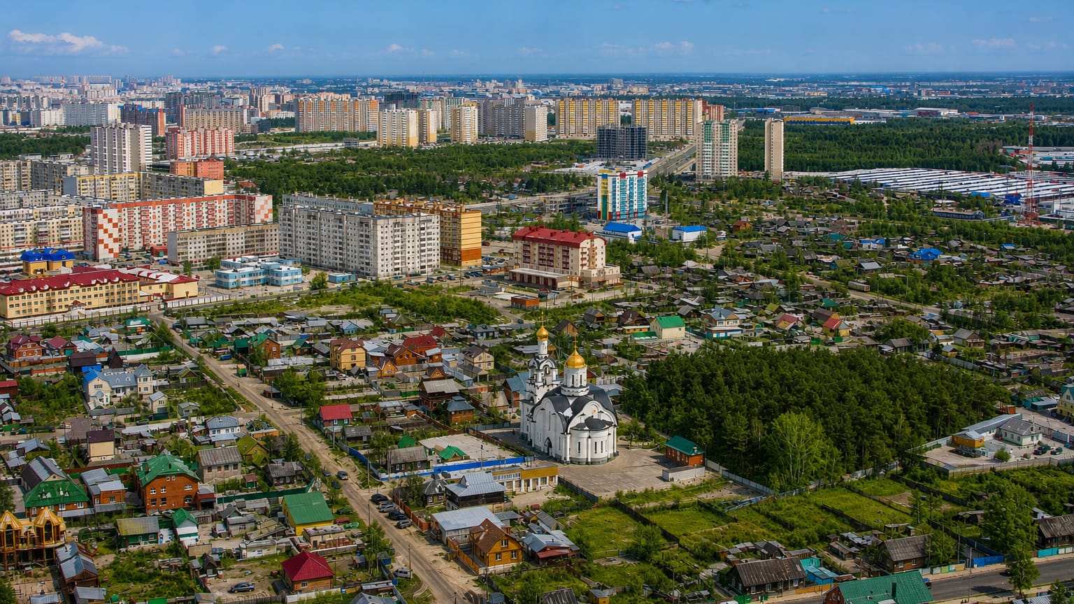Aerial view of Surgut, Russia, with a white golden-domed church, wooden houses and apartment blocks by forest.