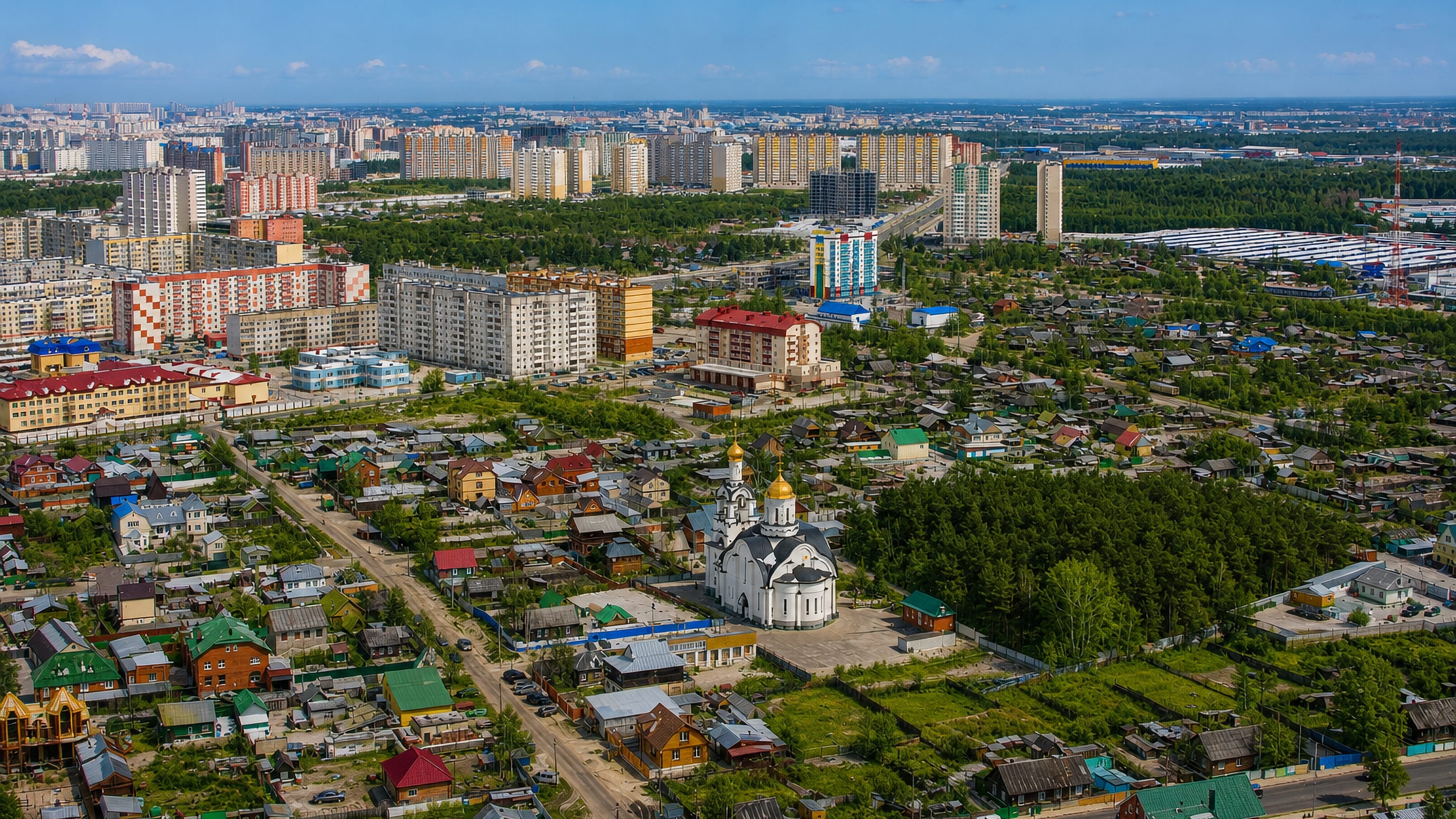 Aerial view of Surgut, Russia, with a white golden-domed church, wooden houses and apartment blocks by forest.