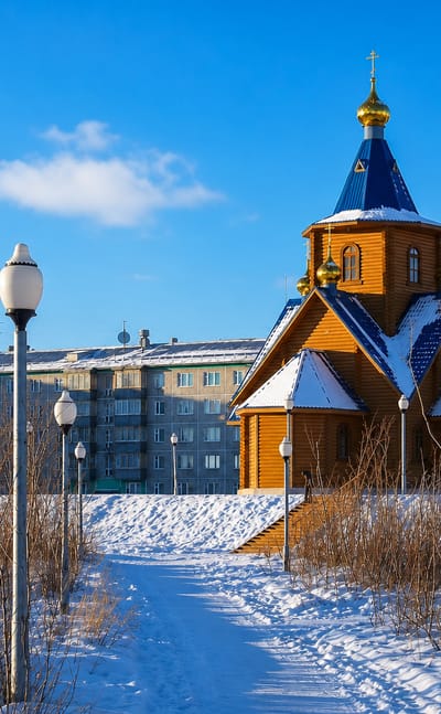 Wooden Orthodox church with blue and gold domes in snowy Vorkuta, Russia, with Soviet-era apartment blocks behind.