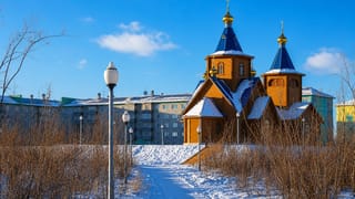 Wooden Orthodox church with blue and gold domes in snowy Vorkuta, Russia, with Soviet-era apartment blocks behind.