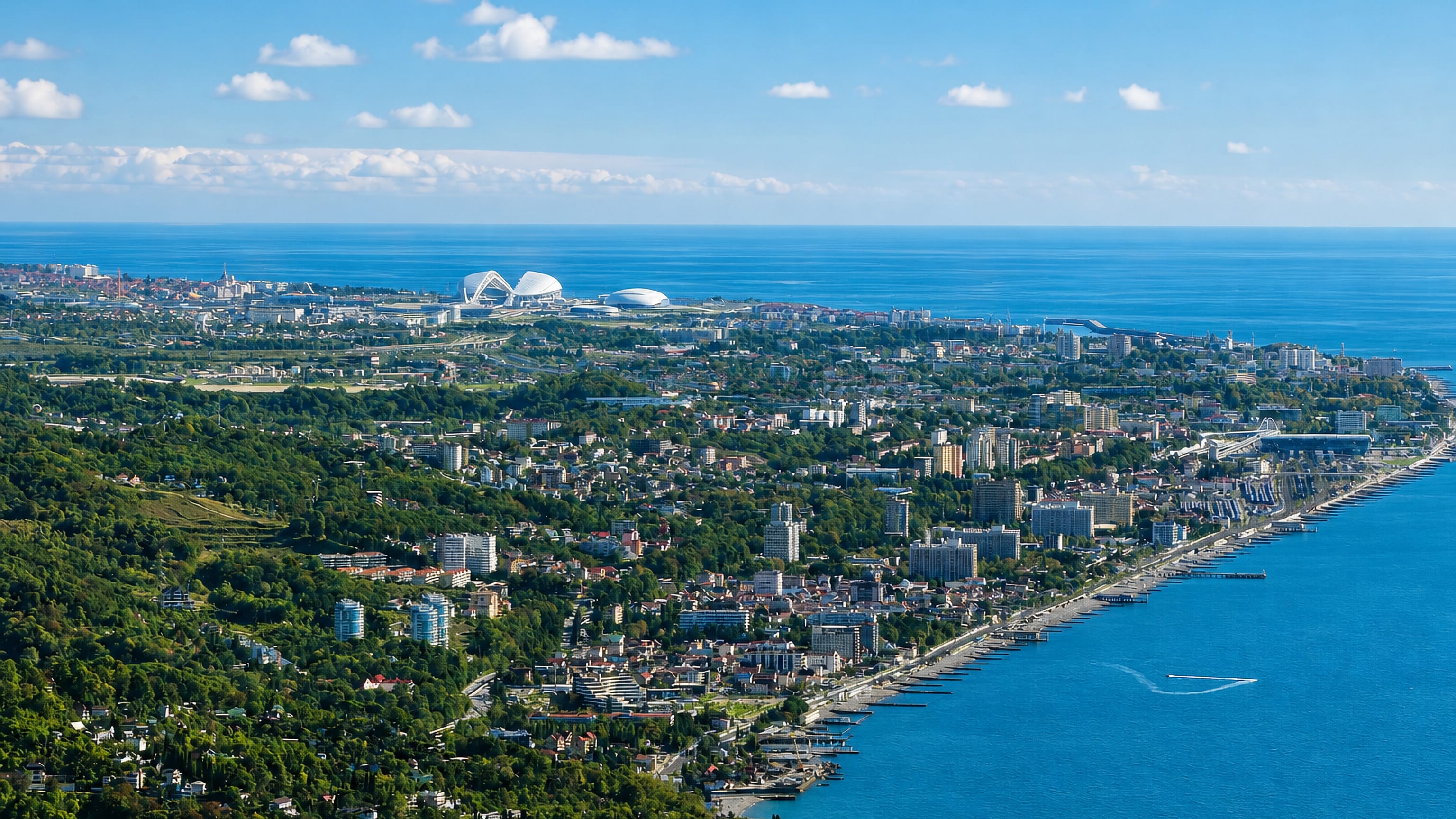 Aerial view over Adler, Russia, with the Black Sea coast, Olympic Park stadiums and wooded hills behind the resort.