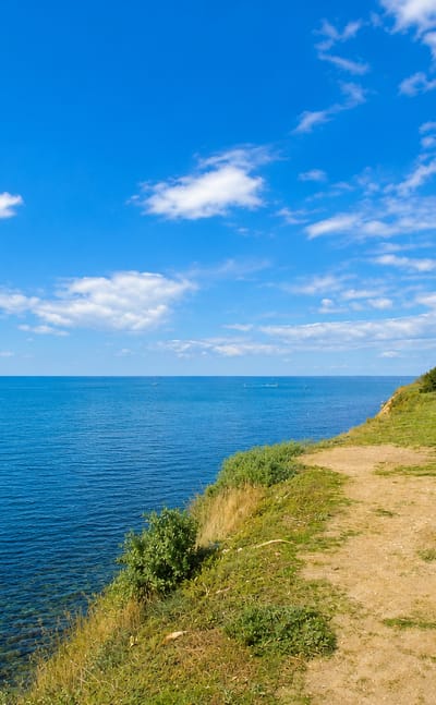 Striped lighthouse on a grassy clifftop above the calm blue Black Sea at the resort town of Anapa, Russia.
