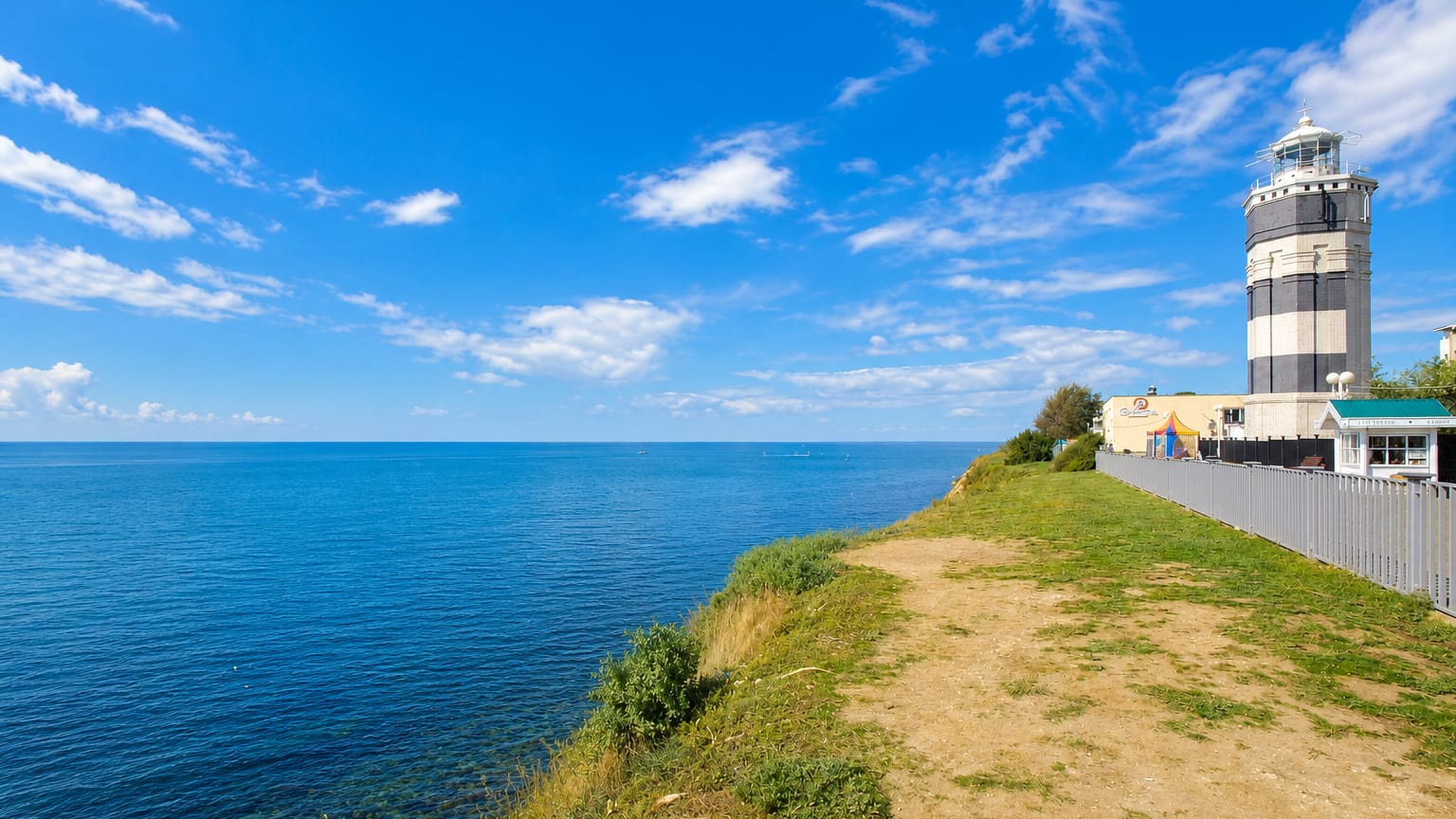 Striped lighthouse on a grassy clifftop above the calm blue Black Sea at the resort town of Anapa, Russia.