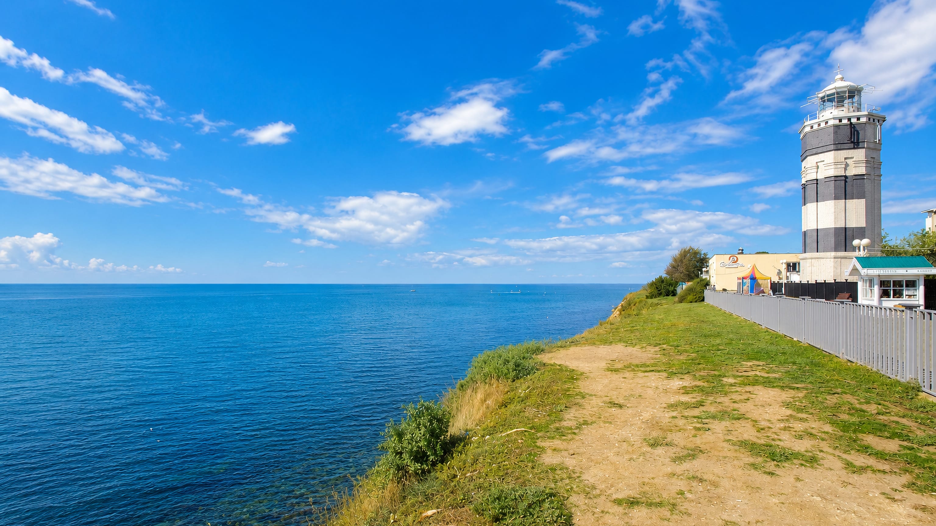 Striped lighthouse on a grassy clifftop above the calm blue Black Sea at the resort town of Anapa, Russia.