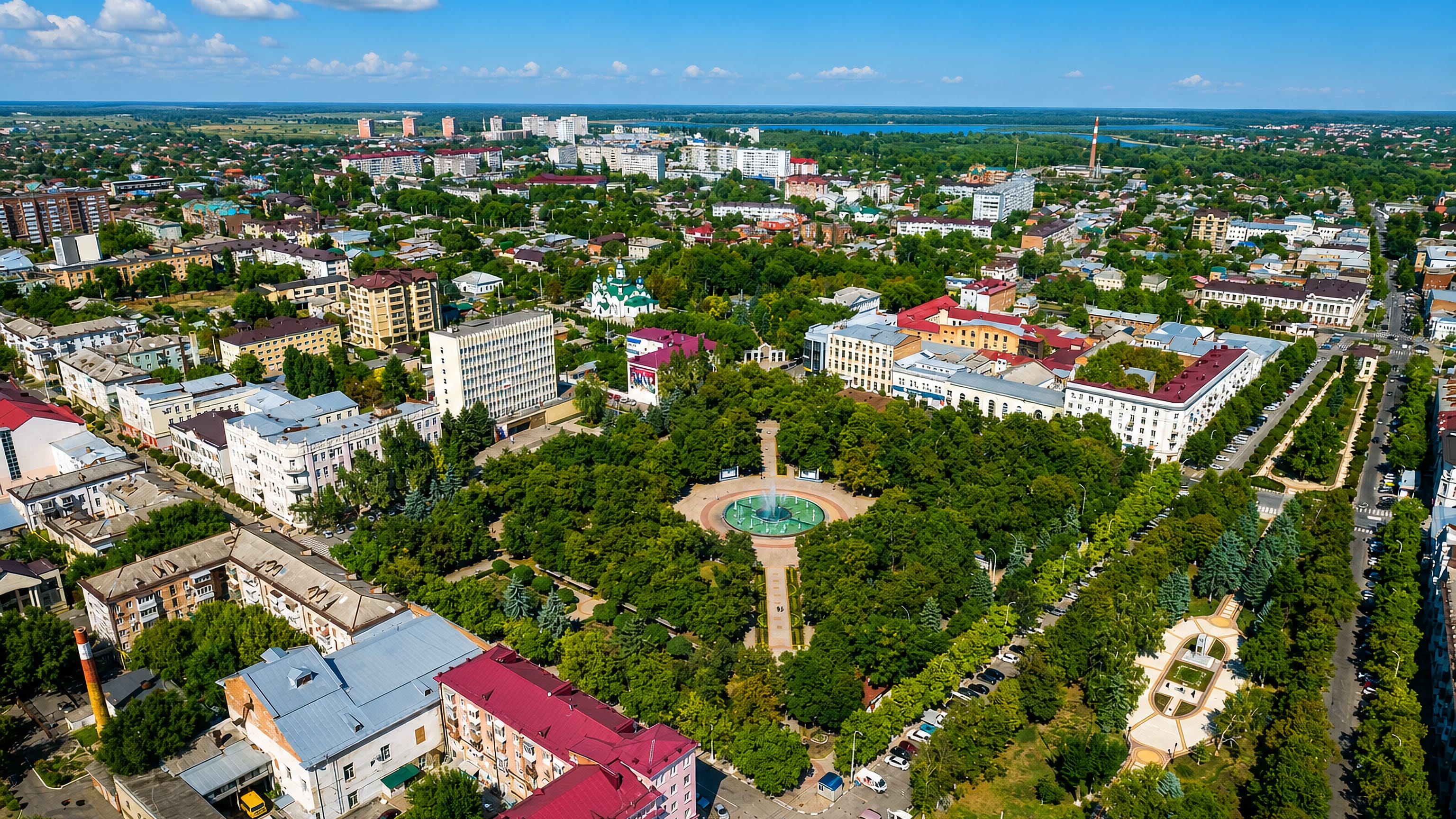 Aerial view of Armavir's central park, fountain plaza and Orthodox church among tree-lined streets.