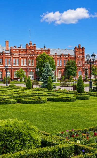 Ornate red-brick 19th-century building with clipped parterre gardens and a fountain in Kropotkin, southern Russia.