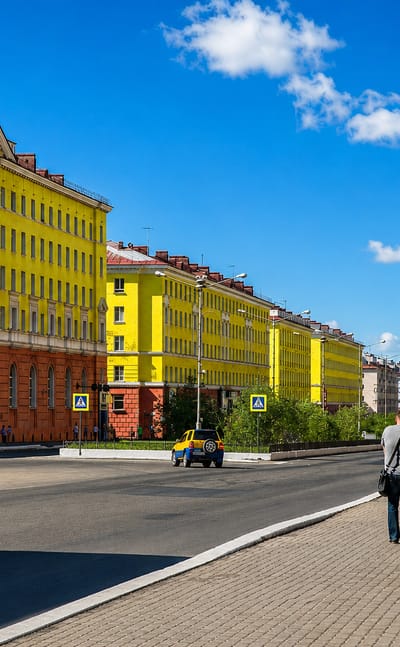 A street in Norilsk lined with colourful Stalinist-era apartment blocks under a blue sky.