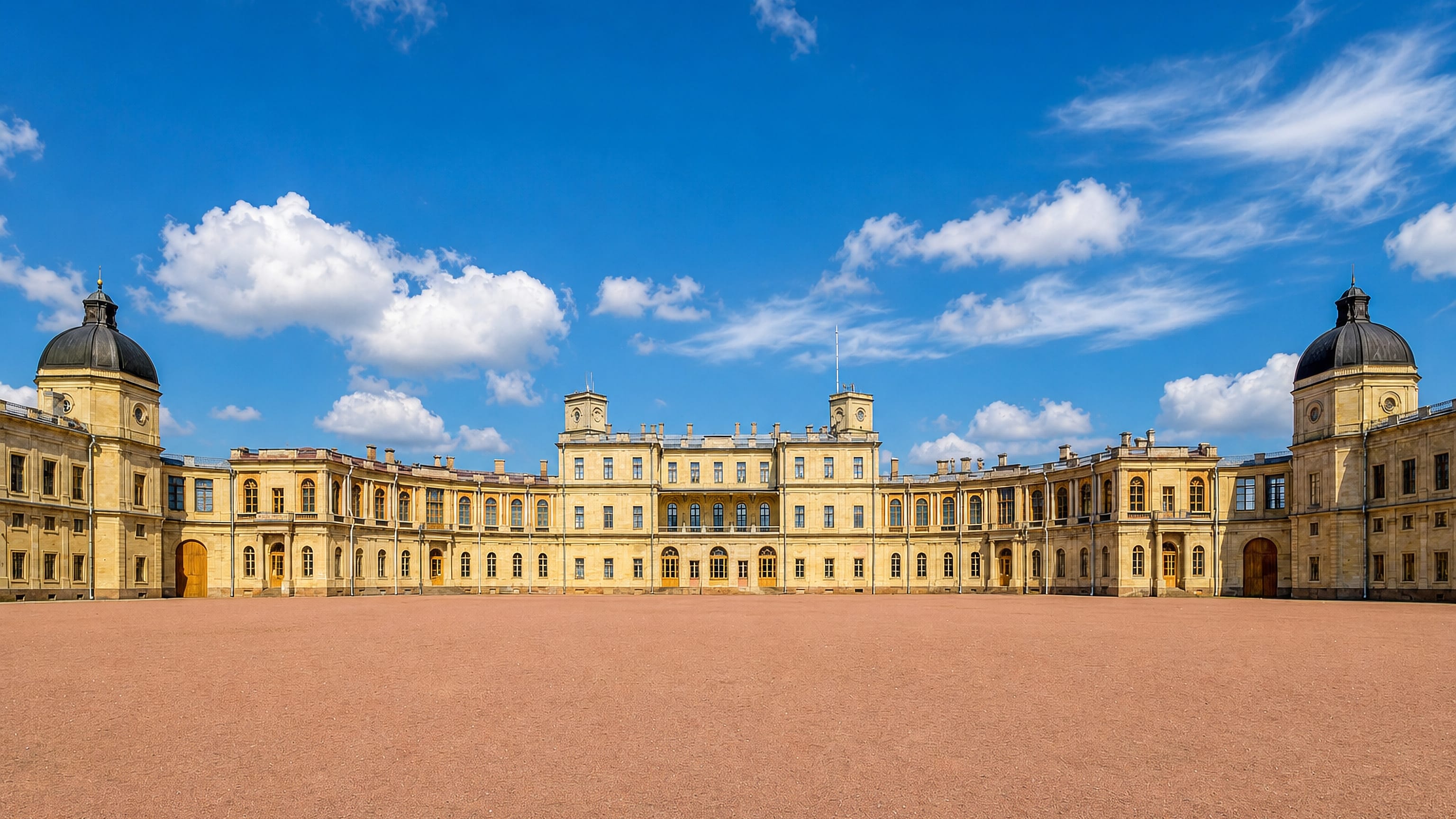 The sandstone facade and twin domed towers of Gatchina Palace rise beyond its broad parade ground.