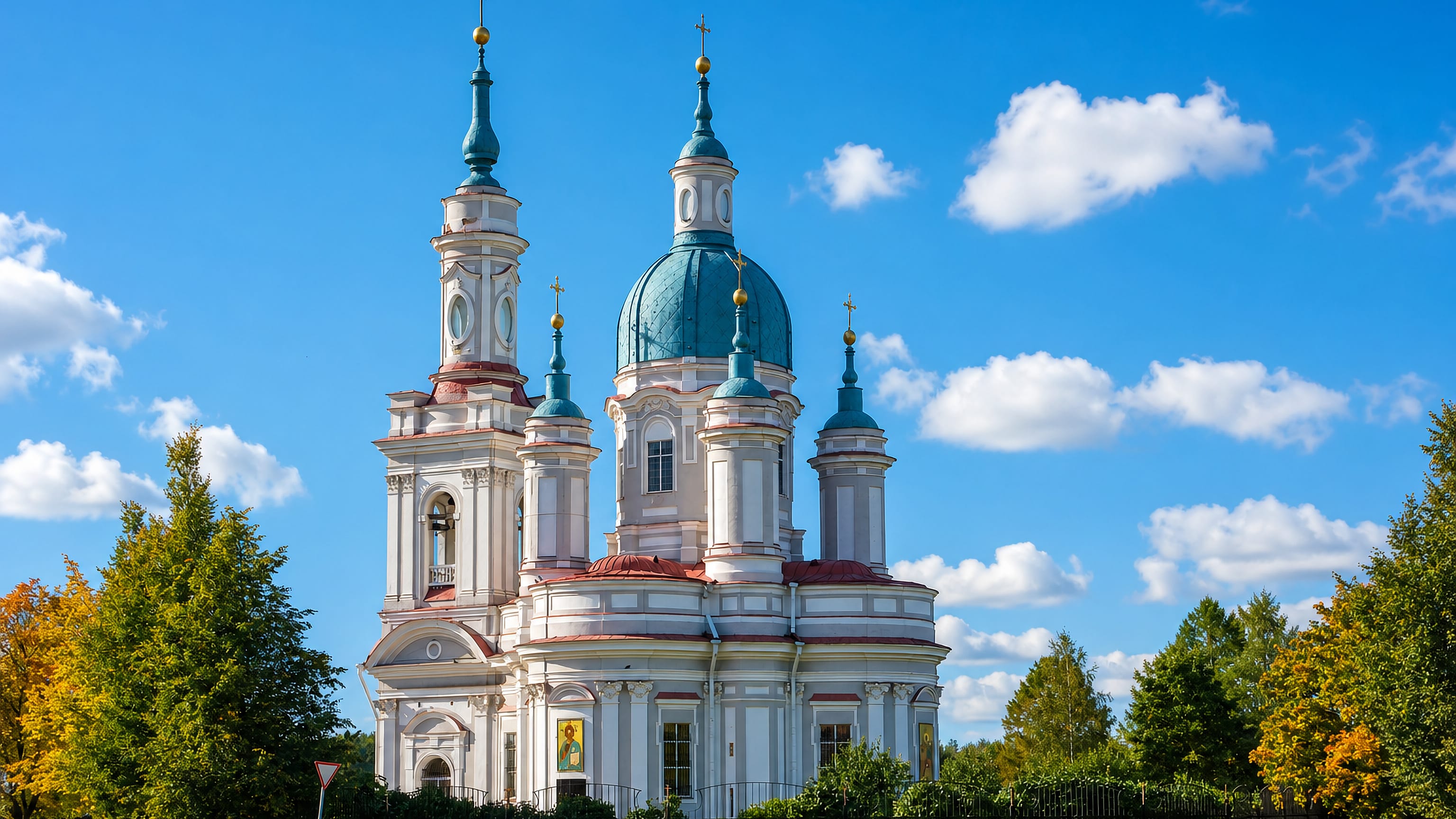 The white baroque Cathedral of St Catherine in Kingisepp, its teal domes and bell tower against blue sky.