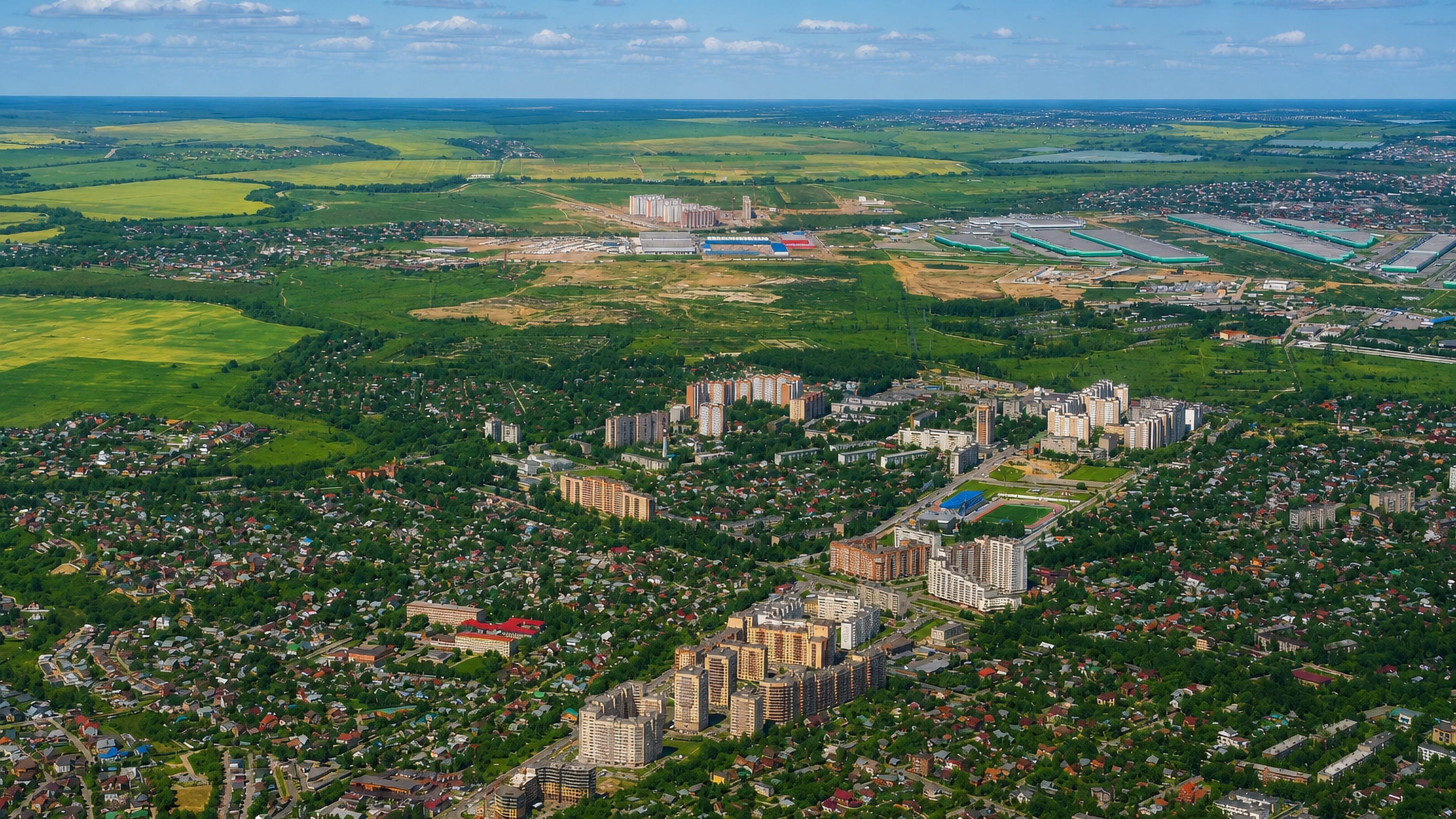 Domodedovo from the air: apartment blocks and dacha streets among woods and fields near Moscow.