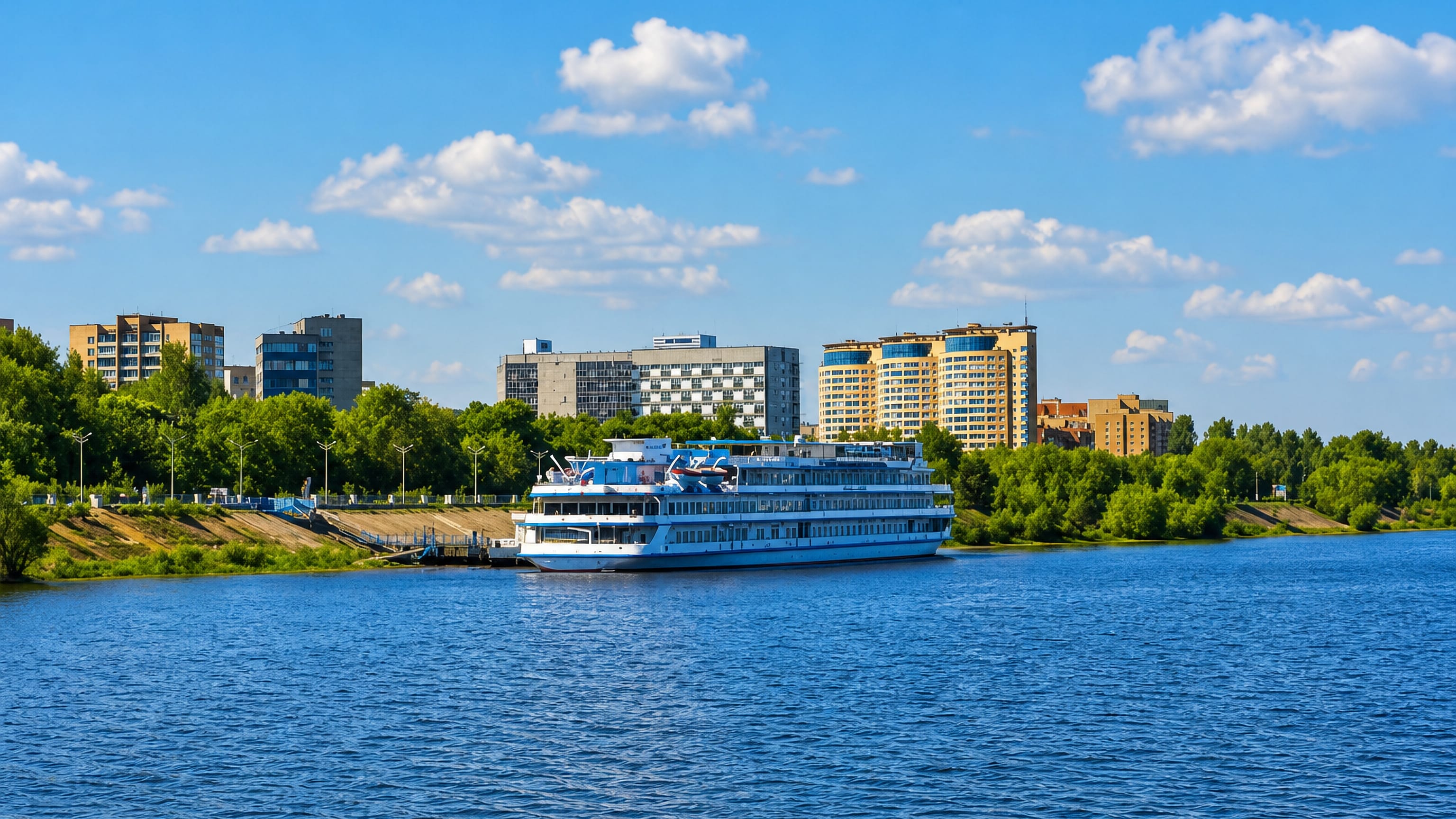 Sunny Volga riverfront at Dubna, Russia, with a white river cruise ship moored below apartment towers