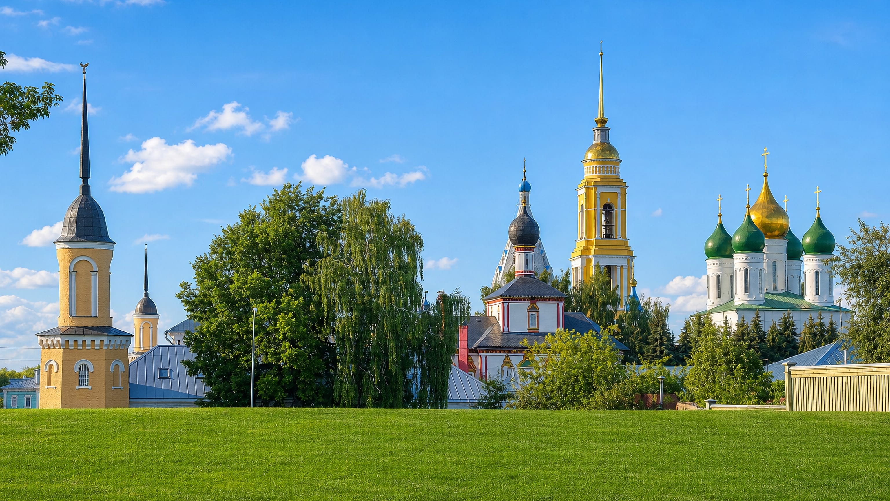 Gold- and green-domed churches and the yellow bell tower of Kolomna's kremlin rising above a green meadow.