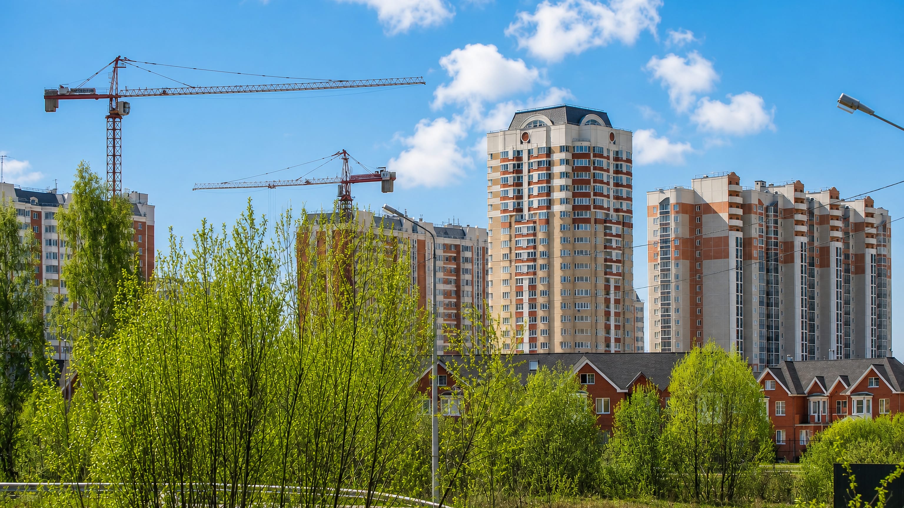New brick high-rise blocks and tower cranes rising above birch scrub and townhouses on the edge of Lobnya.