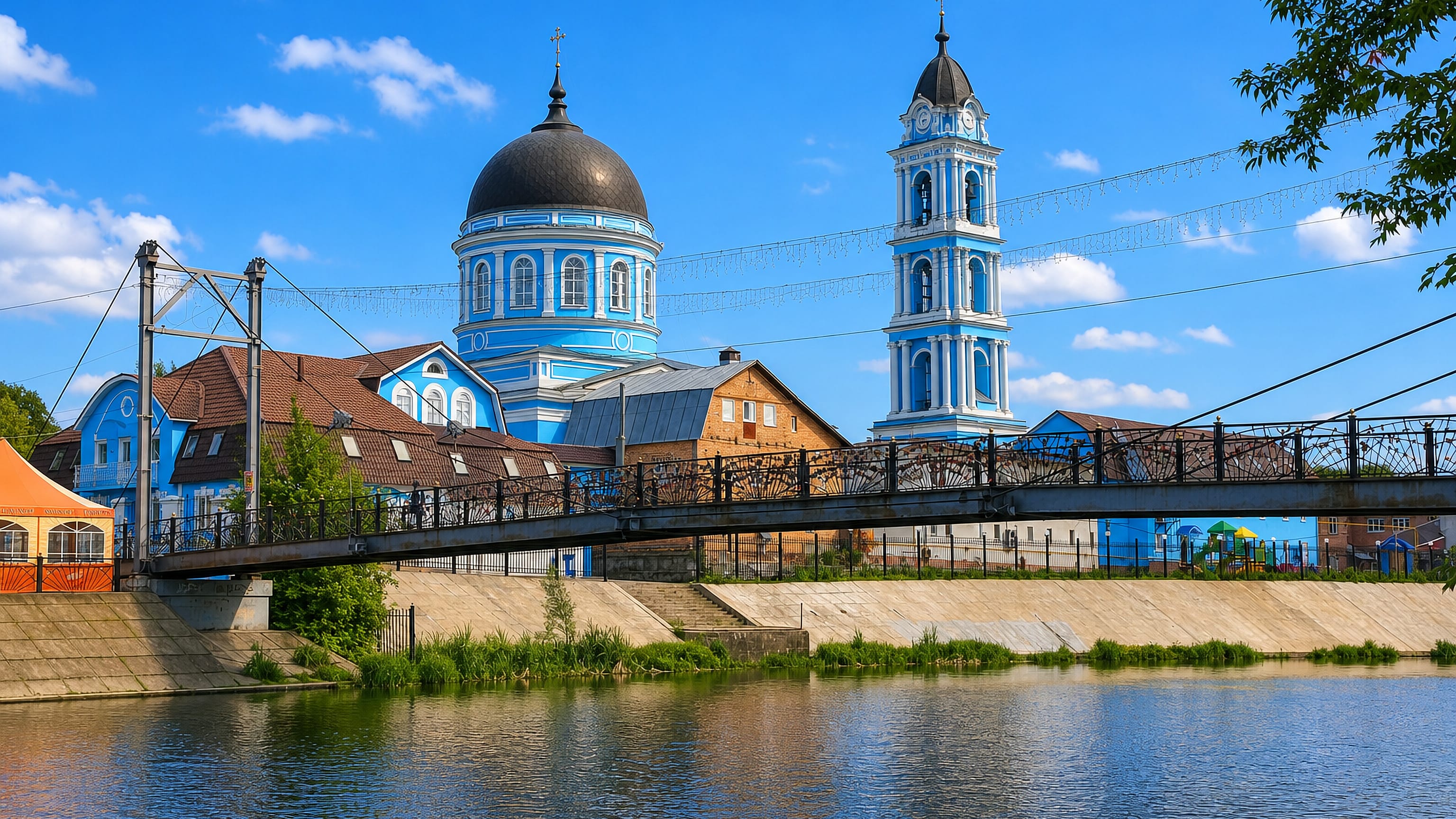 Noginsk's blue Epiphany Cathedral and bell tower above the Klyazma river, seen past a suspension footbridge.