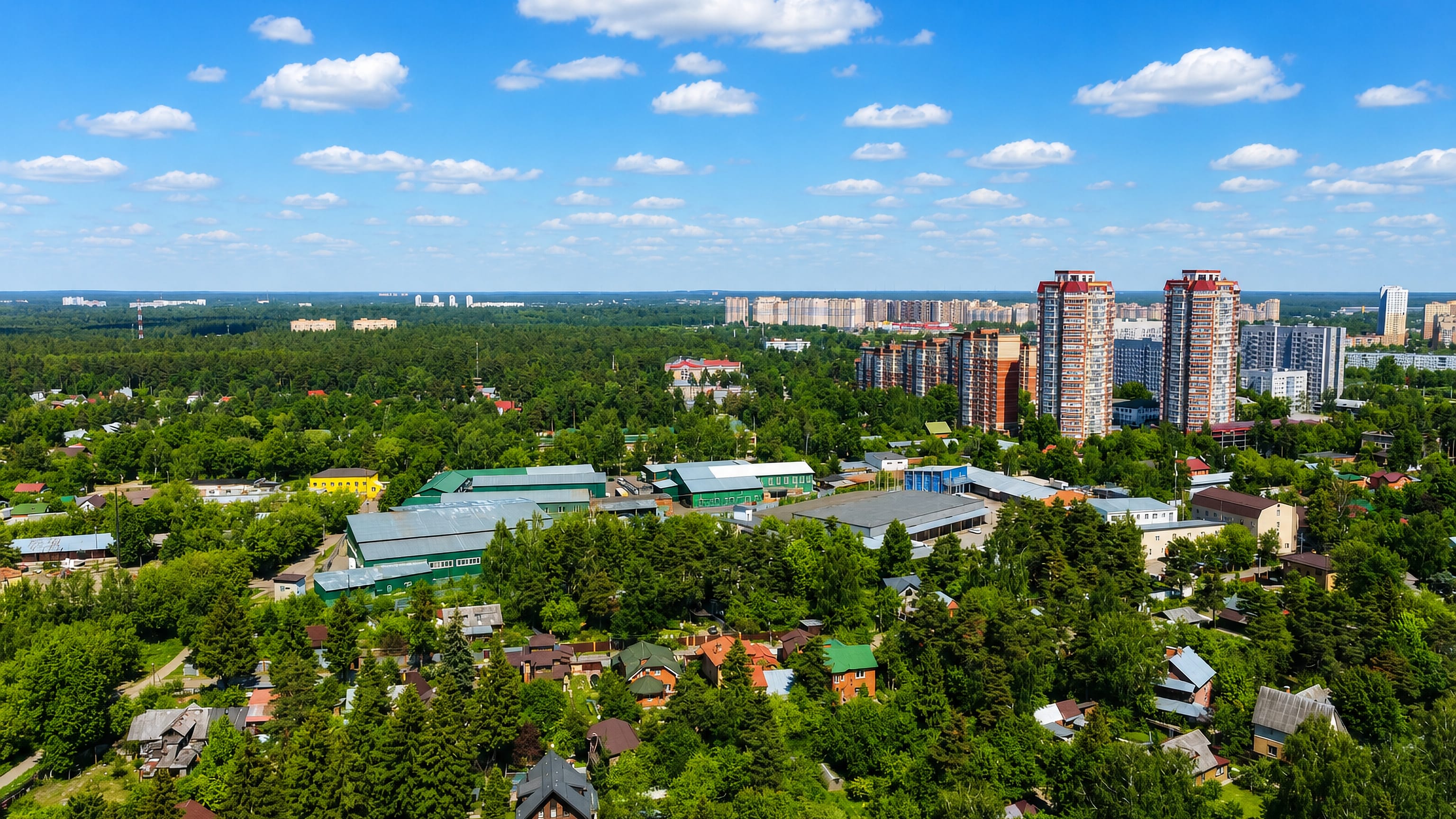 Aerial view of Pushkino, Russia, with pine forest, wooden dachas and modern high-rise apartment towers beyond.