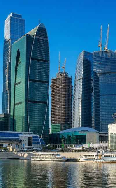 Moscow City skyscraper cluster rising across the Moskva River from Dorogomilovo with river boats and a golden-domed church