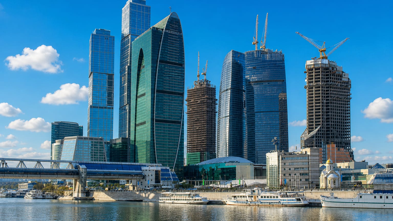 Moscow City skyscraper cluster rising across the Moskva River from Dorogomilovo with river boats and a golden-domed church