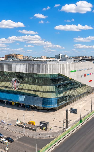 A modern wave-shaped glass commercial building beside a wide highway in Gol'yanovo, Moscow.