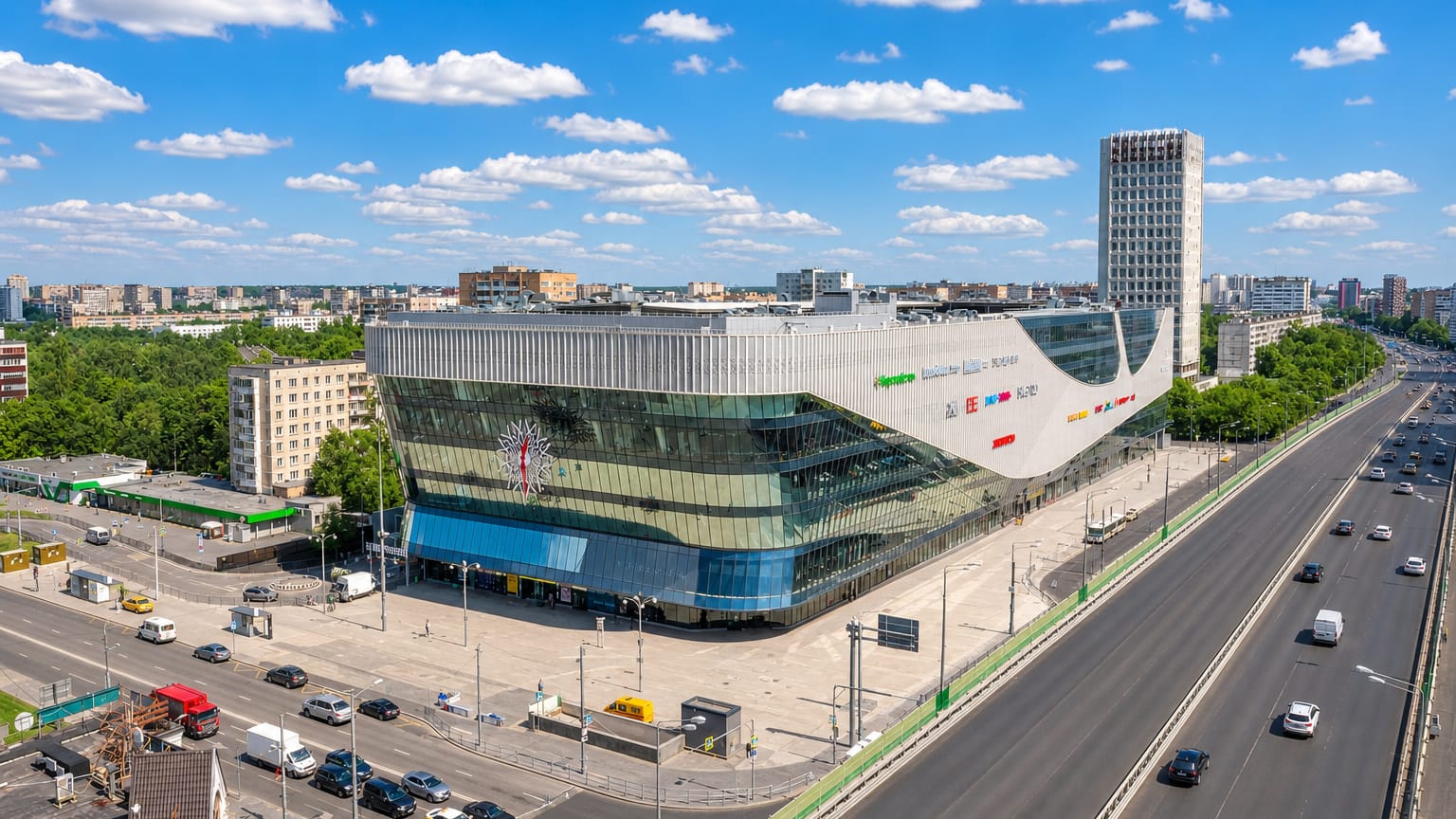 A modern wave-shaped glass commercial building beside a wide highway in Gol'yanovo, Moscow.