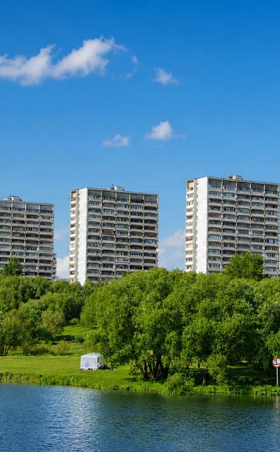 Soviet-era panel high-rise apartment blocks lining a green riverbank in Kapotnya, Moscow