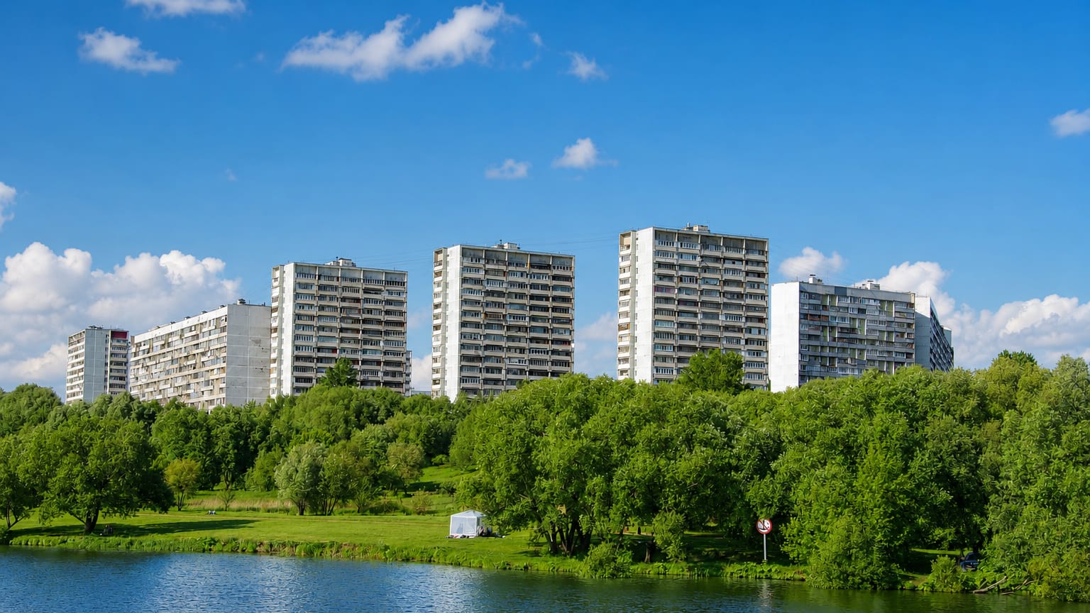 Soviet-era panel high-rise apartment blocks lining a green riverbank in Kapotnya, Moscow